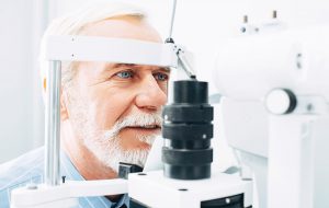 An older man getting his eyes examined at an optometrists office to check for eye diseases.