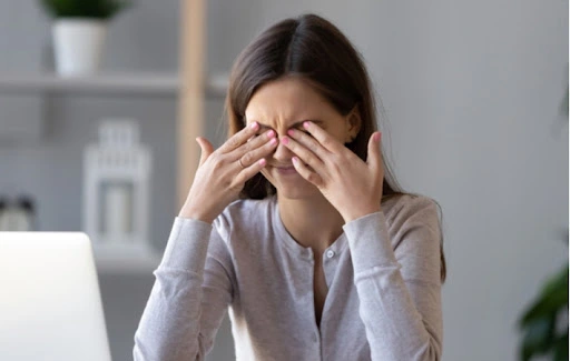 A woman sitting at her computer rubs her eyes due to dryness.