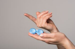 A woman holding a contact lens case in her left hand, and a contact lens is sitting on her right index finger