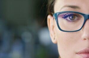 A close up image of a woman's face and she is wearing blue glasses