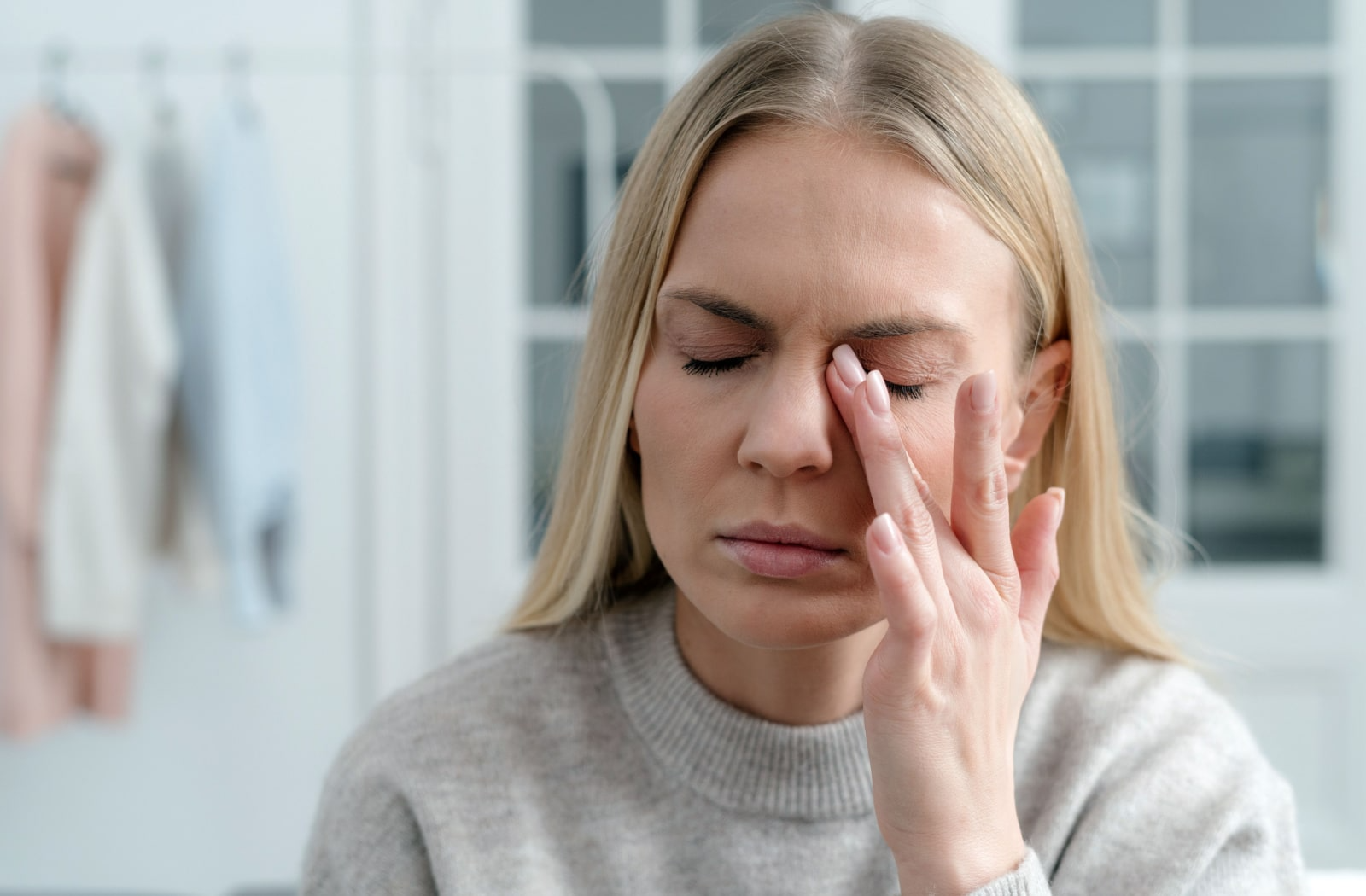 A woman holds her index finger near her eyes due to dry eye pain