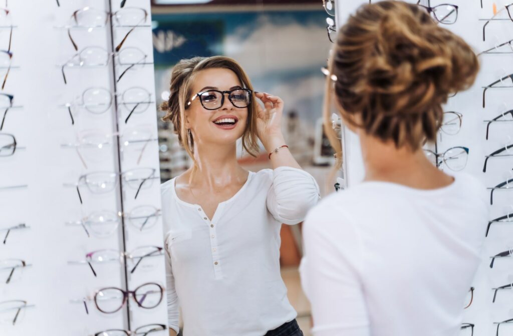 A woman looks at herself in the mirror while she tries on new pairs of glasses at the optometrist's office.