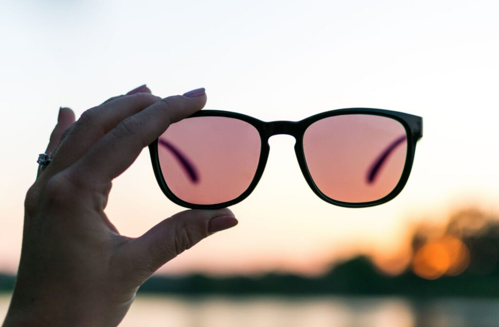 Polarized Sunglasses being held by female hand with sunset in background.