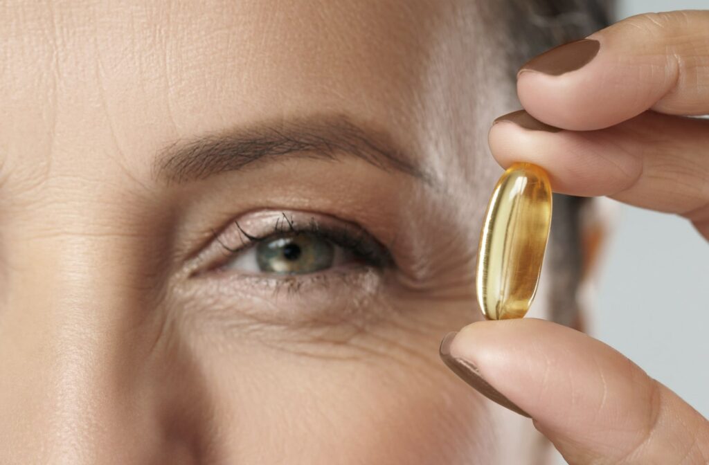 A close up of a woman holding a capsule of fish oil, a source of omega-3 fatty acids, next to her eye