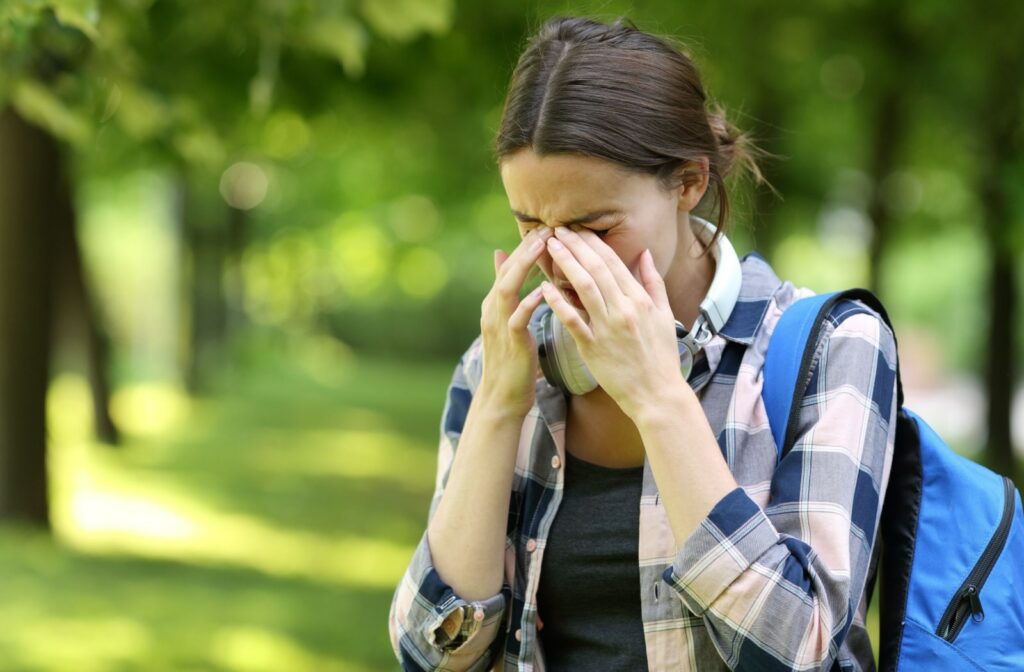A woman rubbing her eyes to alleviate eye dryness that is possibly caused by allergies.