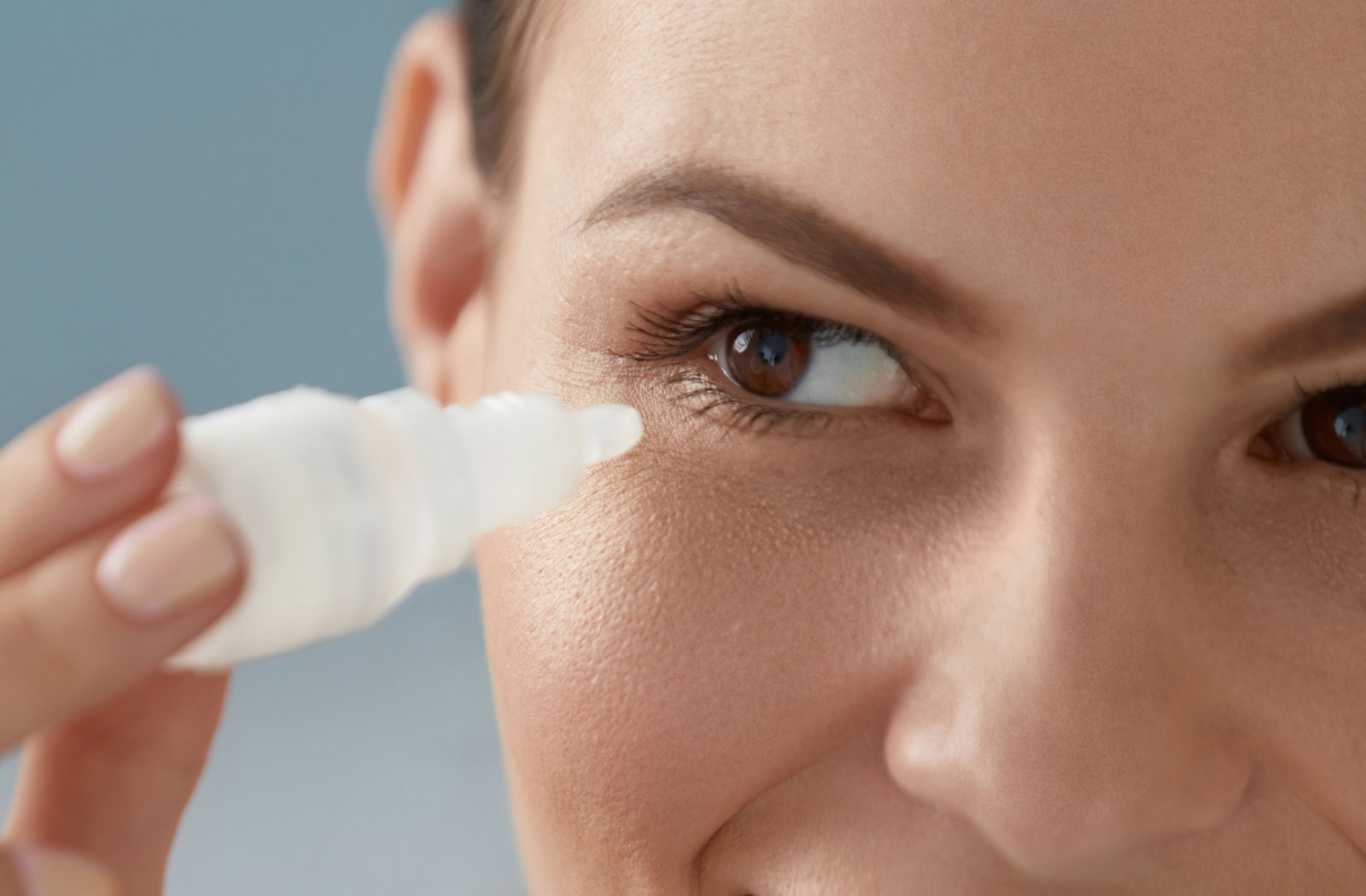 An adult holds eye drops up to their dry eyes, preparing to insert the drops.