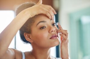 Woman with hair in a bun putting contact lens in left eye.