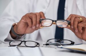 Optometrist’s hands holding a pair of glasses with multiple frames displayed on the table.