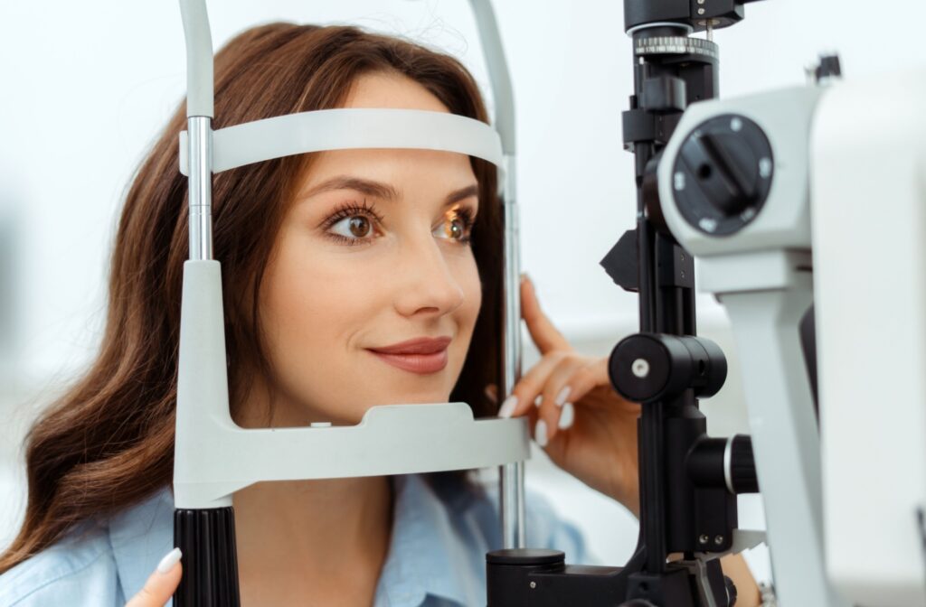 A person sits at a slit lamp during an eye exam, looking into the device while holding the side handles.